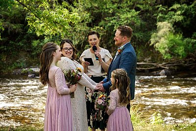 couple getting married by river with flower girls.