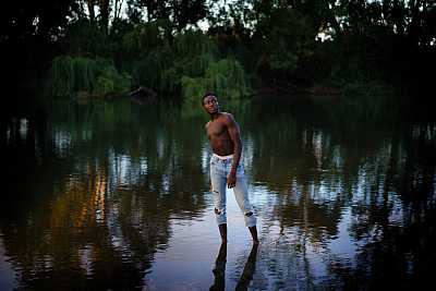 Young man standing in river with his shirt off.